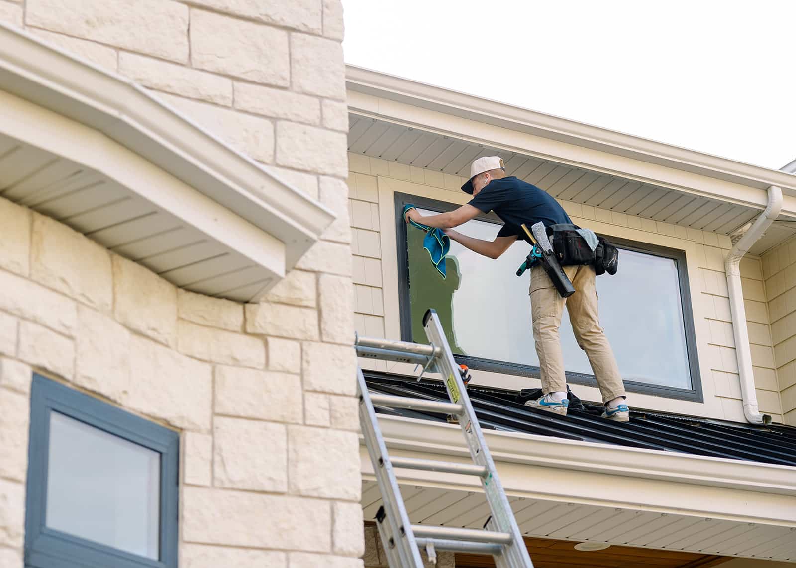 A professional window cleaner on a ladder cleaning a residential window in Logan, Utah. The cleaner uses a squeegee and cloth for sparkling results.